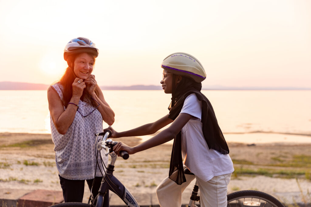 A mentor puts on a mentor while a young mentee in a hijab rides a bicycle